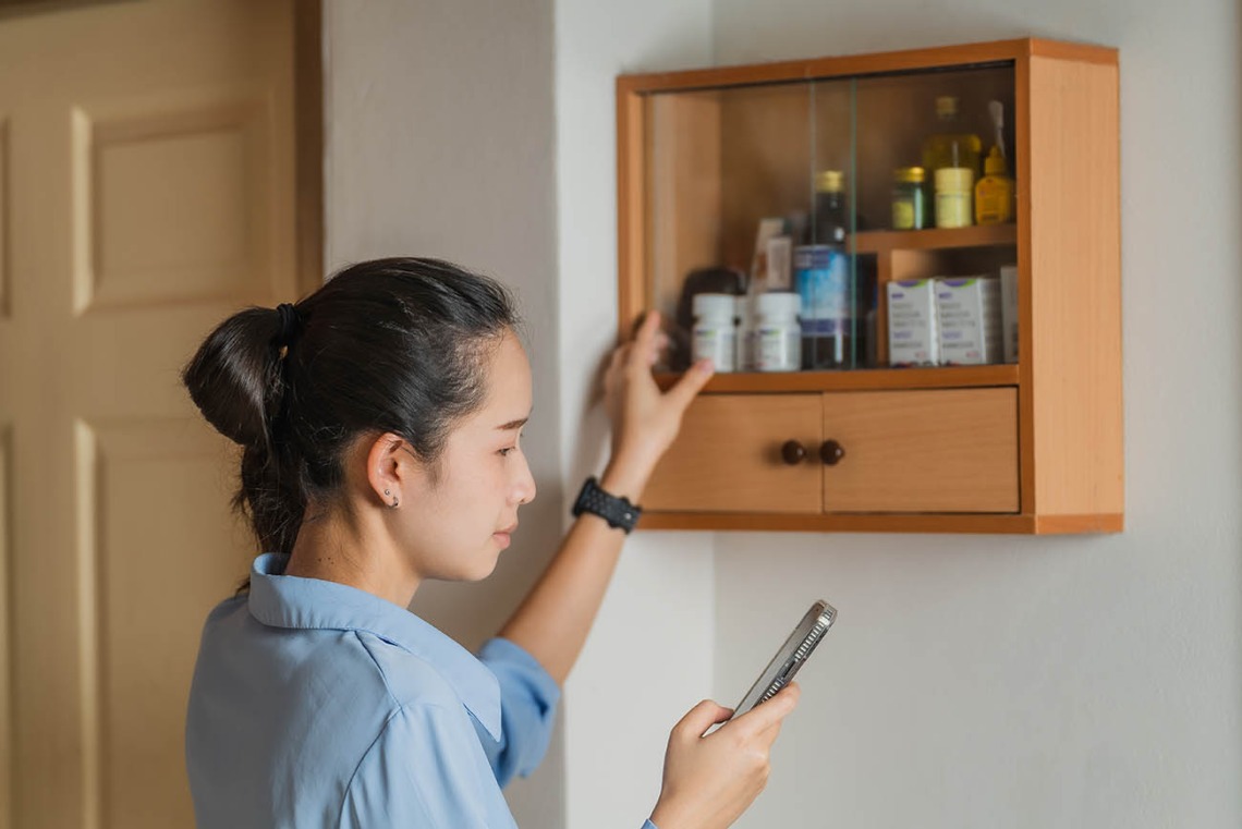 Woman looks into medicine cabinet while consulting her phone.