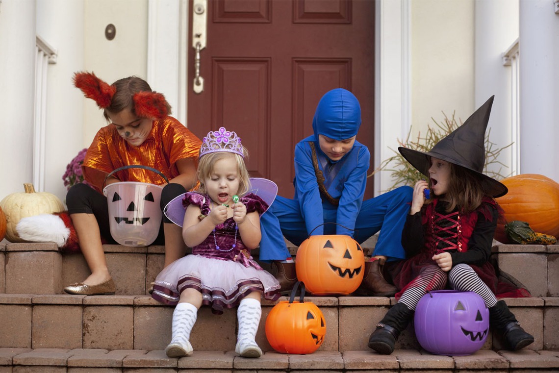 Group of costumed kids sitting in front of excitedly looking through Halloween candy
