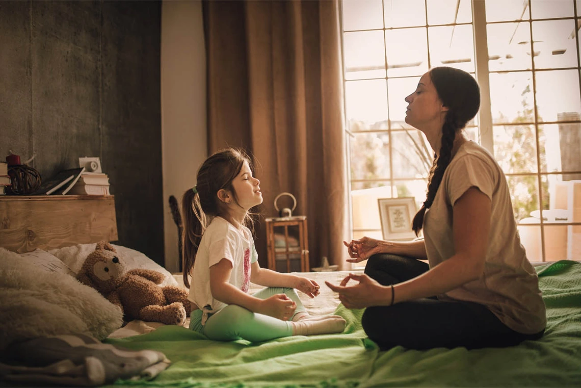 Girl and woman facing each other on a bed and meditating