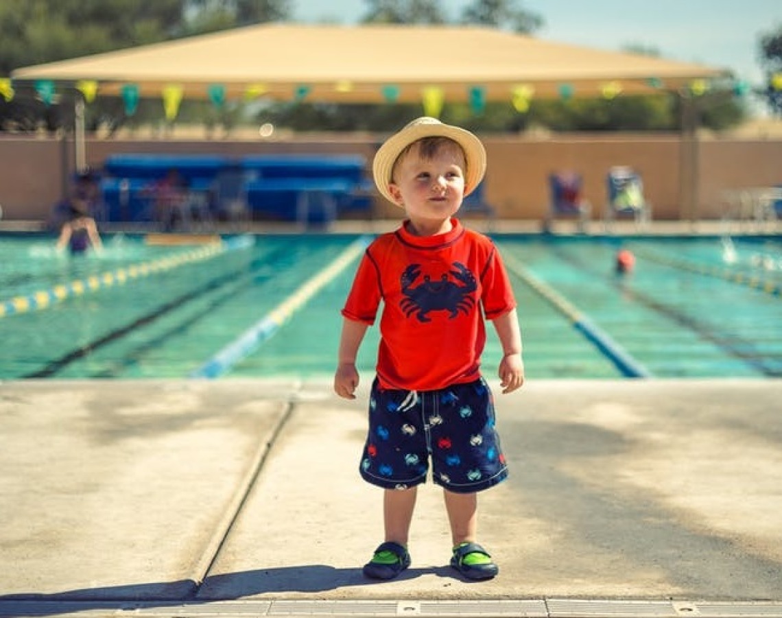 Little boy wearing by a pool wearing sun protective clothing.