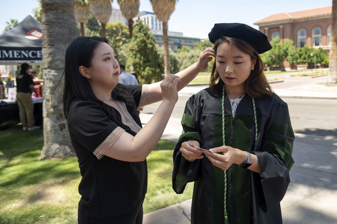 Lydia Lee (left) helps her sister, Eun Hye Lee, MD, with her cap before the start of the College of Medicine – Tucson class of 2022 convocation at Centennial Hall. 