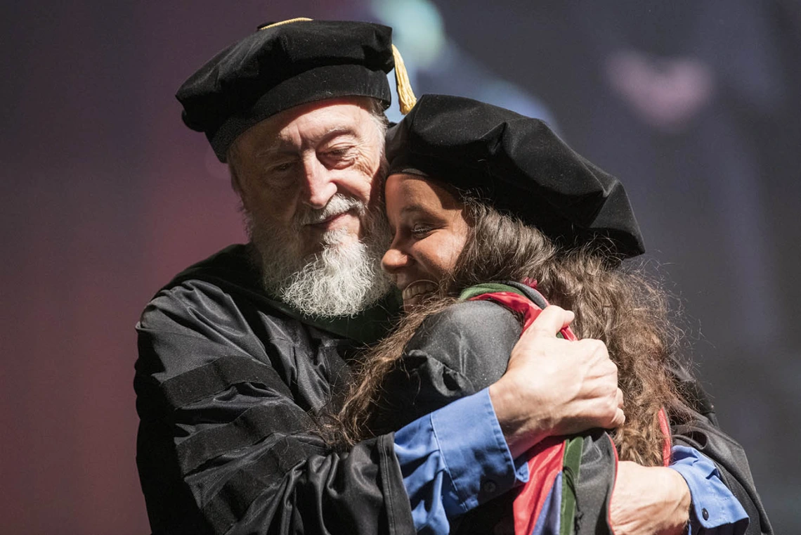 Retired professor Craig McClure, MD, hugs Faith Dickerson, MD, after hooding her during the College of Medicine – Tucson class of 2022 convocation at Centennial Hall. 