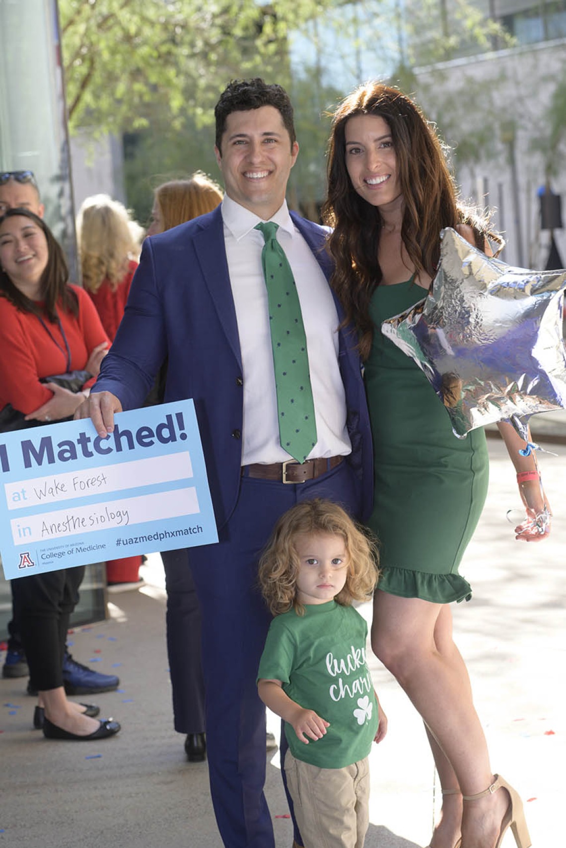 A light skinned man in a suite with his wife and child smile. He holds a poster that says "I Matched"