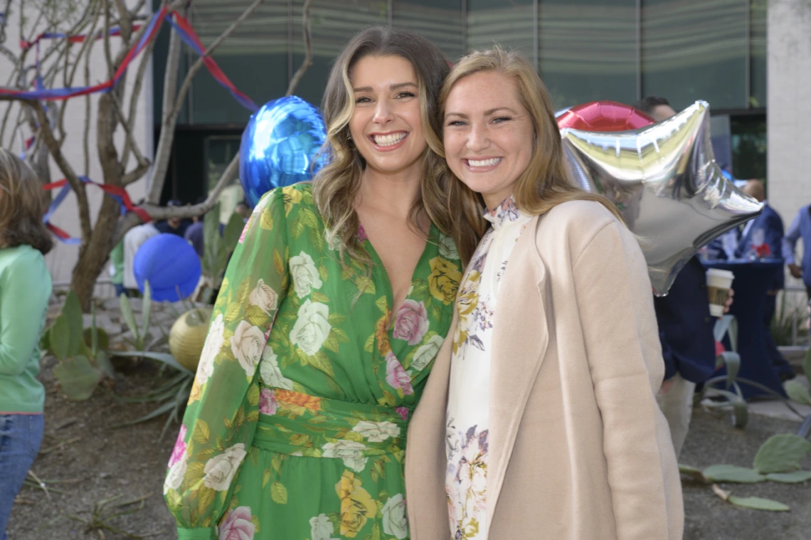 Two young adult women hug sideways and smile. 