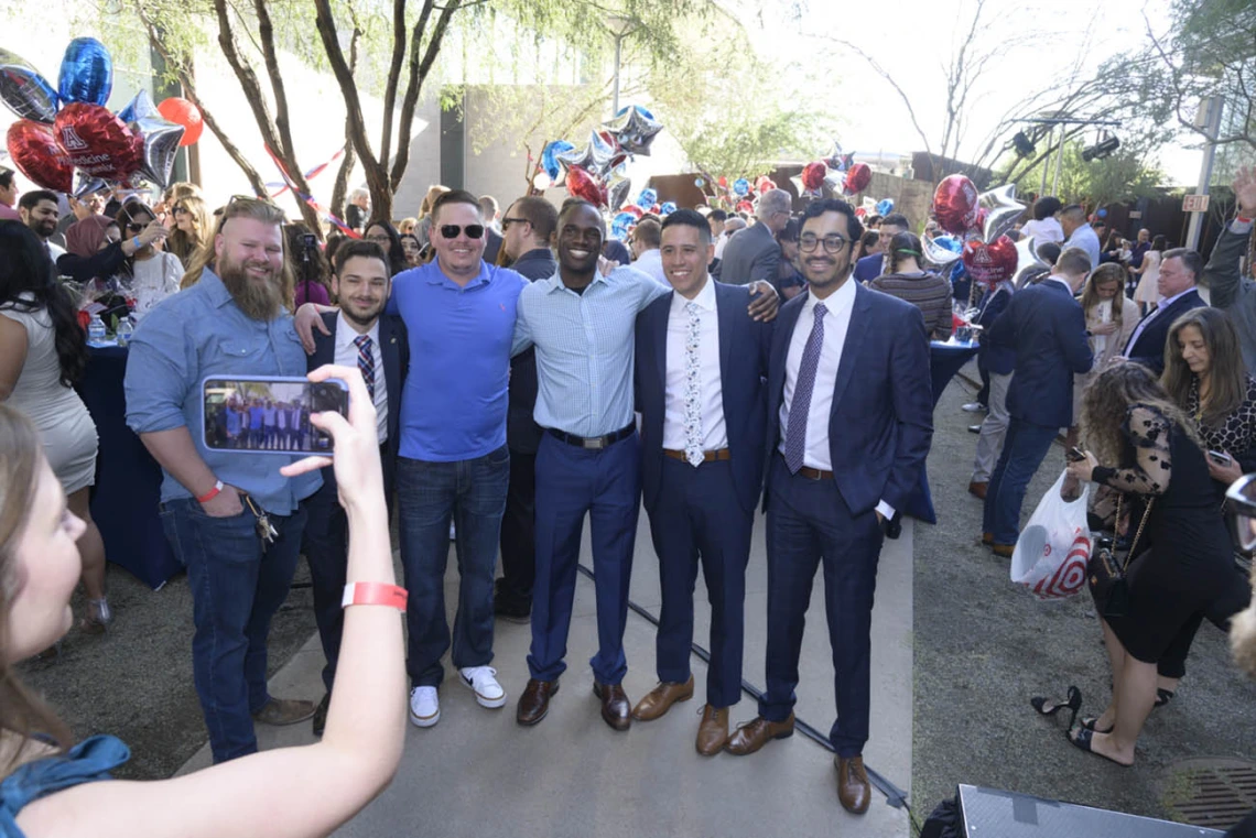 Six young adult men stand side by side with arms around each others shoulders. 