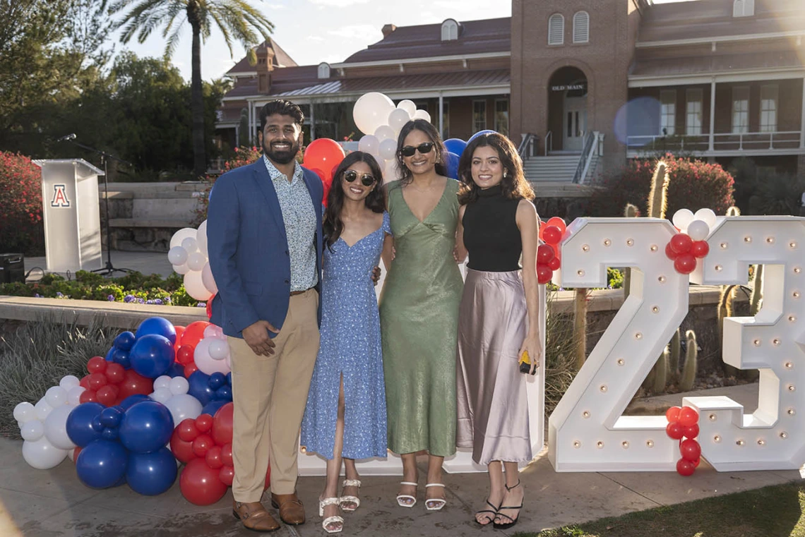 Four people with brown skin stand in front of a large 2023 sign smiling with their arms around each other.