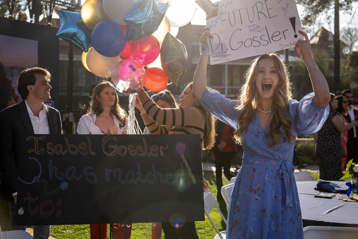 Young woman in blue dress smiling big holds a sign that reads "Future Dr. Gossler"