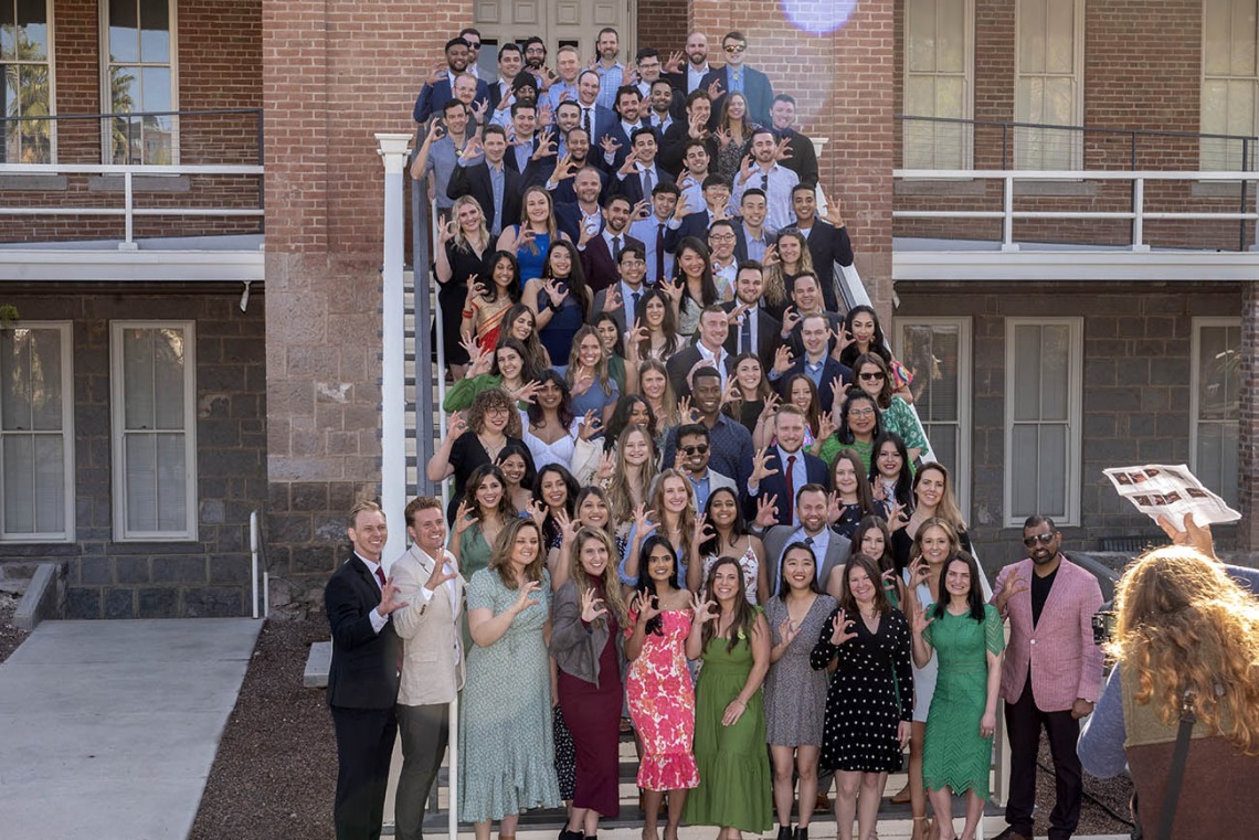 100-plus medical students pose on the stairs while people take photographs. 
