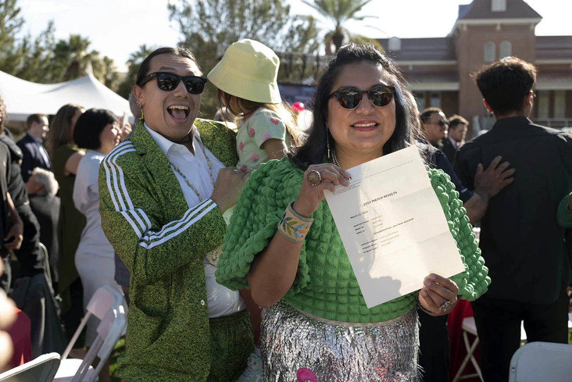 A woman in sun glasses holds a letter while smiling and her husband and child are in the background. 