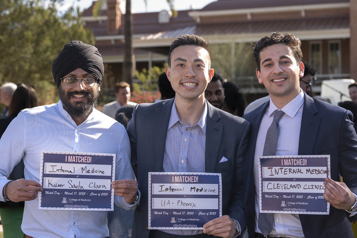 Three young adult men, all smiling, stand in a row holding signs stating where they were matched. 