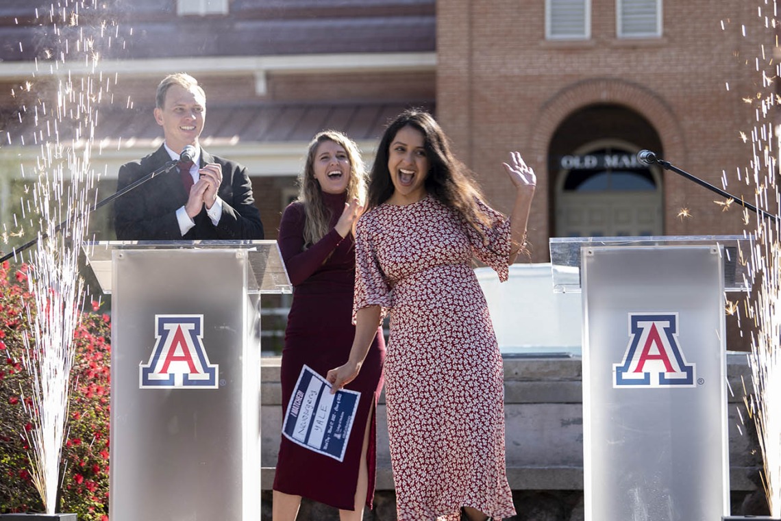 Young woman with long dark hear in a dress cheers in front of two podiums with Arizona As on them.