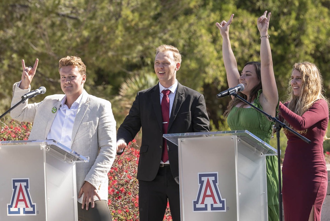 A young adult man and woman each stand at an Arizona podium with arms and hands raised in celebration. 