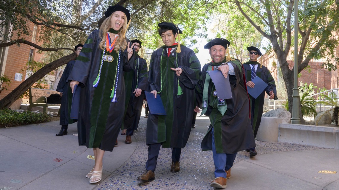 Several pharmacy students in graduation regalia smile as they walk outside after their graduation ceremony.