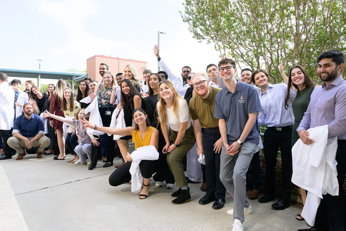 A large group of medical students stand in a line outside smiling and waving. 