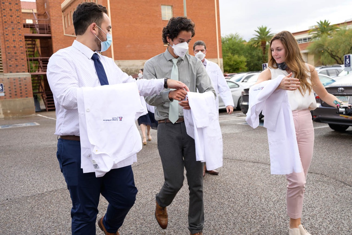 Members of the UArizona College of Medicine – Tucson Class of 2026 discuss how to properly fold their coats as they walk to the ceremony at Centennial Hall.