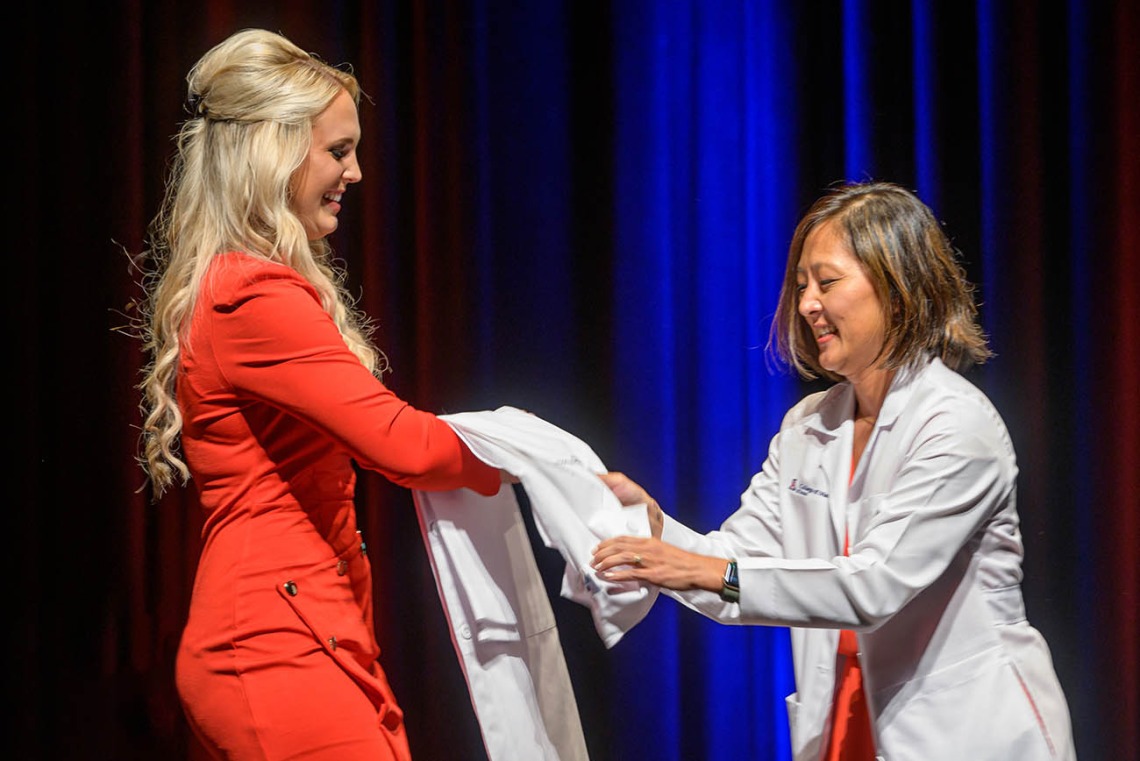 Hailey Patterson prepares to be coated by Alice Min, MD, FACEP, associate dean for career development, at the UArizona College of Medicine – Tucson Class of 2026 white coat ceremony. 