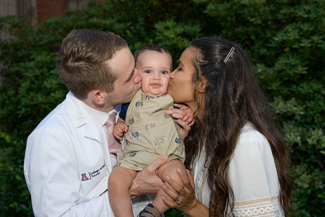 Spencer Holmes and his wife, Aiysha Holmes, celebrate his new white coat by kissing their baby, Eli, after the UArizona College of Medicine – Tucson Class of 2026 white coat ceremony.