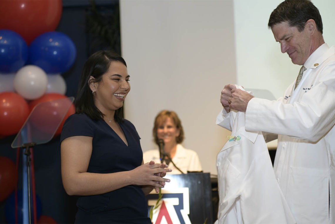 Brenda Valencia Gonzales is presented her white coat by Kevin Moynahan, MD, FACP, vice dean of education at the UArizona College of Medicine – Tucson. 