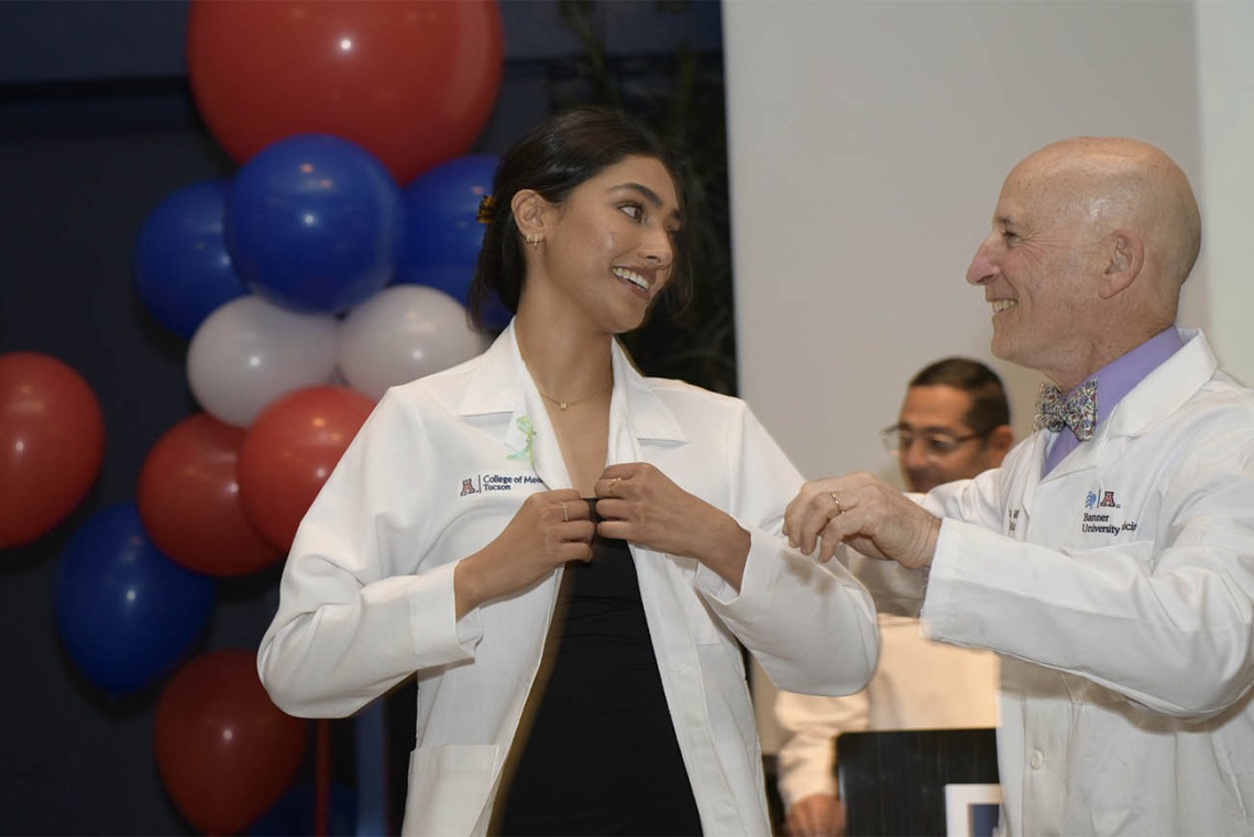 Meghana Partha puts her white coat on after it was presented to her by Paul Gordon, MD, MPH, co-director, Bachelor of Science in Medicine, at the UArizona College of Medicine – Tucson.