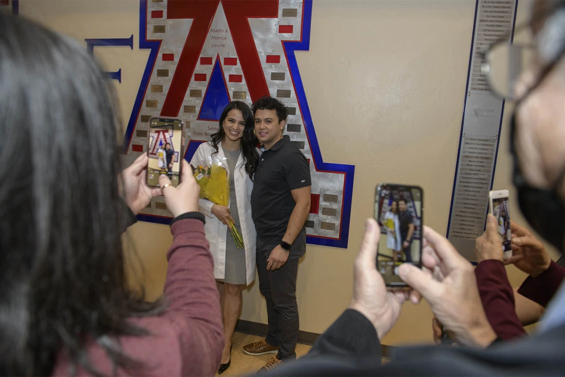 Lupita Molina poses in her new white coat with Blaze Rose as family members take photos after the UArizona College of Medicine – Tucson’s class of 2024 white coat ceremony.