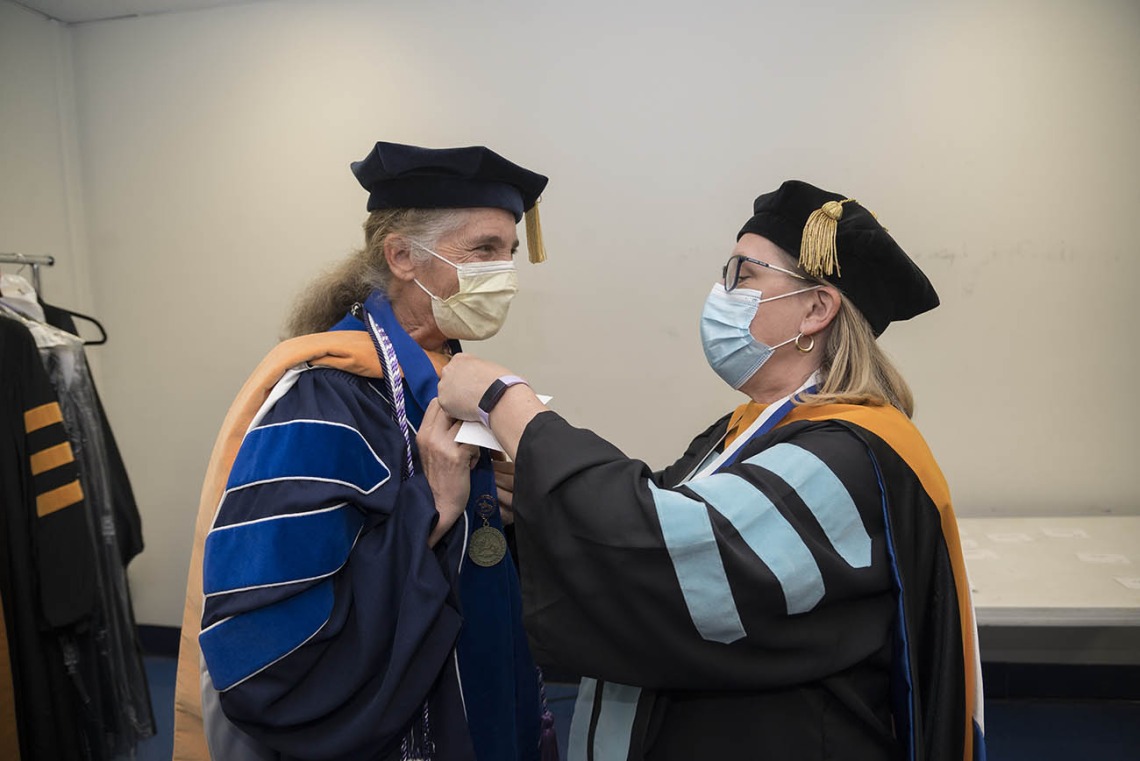 Lisa Kiser, DNP, MSN, (left) is helped with her hood by Erin McMahon, EdD, CNM, FACNM, before the start of the UArizona College of Nursing 2022 spring convocation at Centennial Hall. 