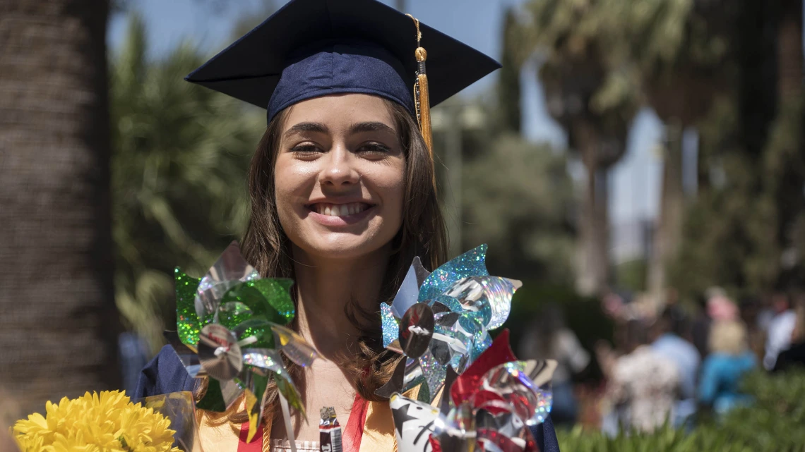 Joanna Schneider poses for a graduation photo with her flowers and pinwheels after receiving her Bachelor of Science in Nursing during the College of Nursing 2022 spring convocation at Centennial Hall.