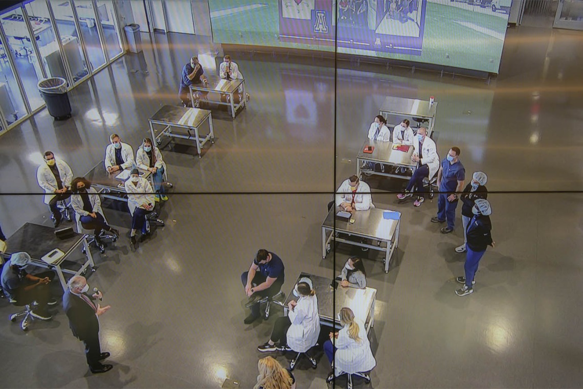 University of Arizona President Robert C. Robbins, MD, (lower left) as seen through four monitors in the Arizona Simulation Technology and Education Center control room, speaks with the second-year CRNA students and faculty between simulations for their clinical skills intensive.  