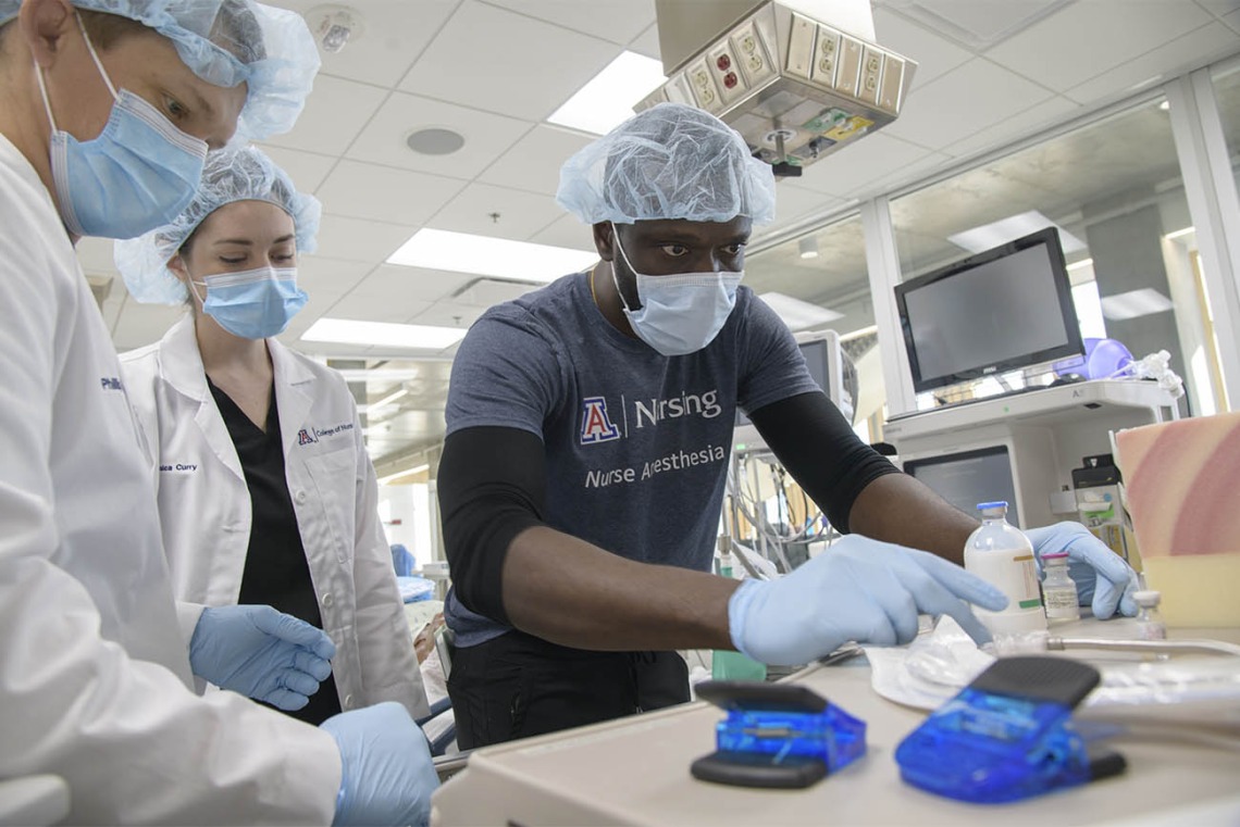 CRNA students Olu Bello, RN, (right) grabs medication to administer to the “patient” while Anastasia Connelly, RN, and Phillip Bullington, RN, keep an eye on the monitor during a critical skills simulation in the Arizona Simulation Technology and Education Center.