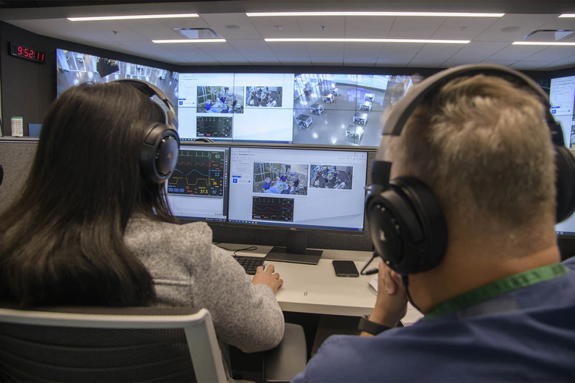 The critical skills simulation for the CRNA students is run from the Arizona Simulation Technology and Education Center control room, where staff member Merryl Lopido (left) and Christopher Herring, DNP, CRNA, assistant director nurse anesthesiology, control the high-tech manikin’s vitals and responses as the students work to stabilize the “patient.”