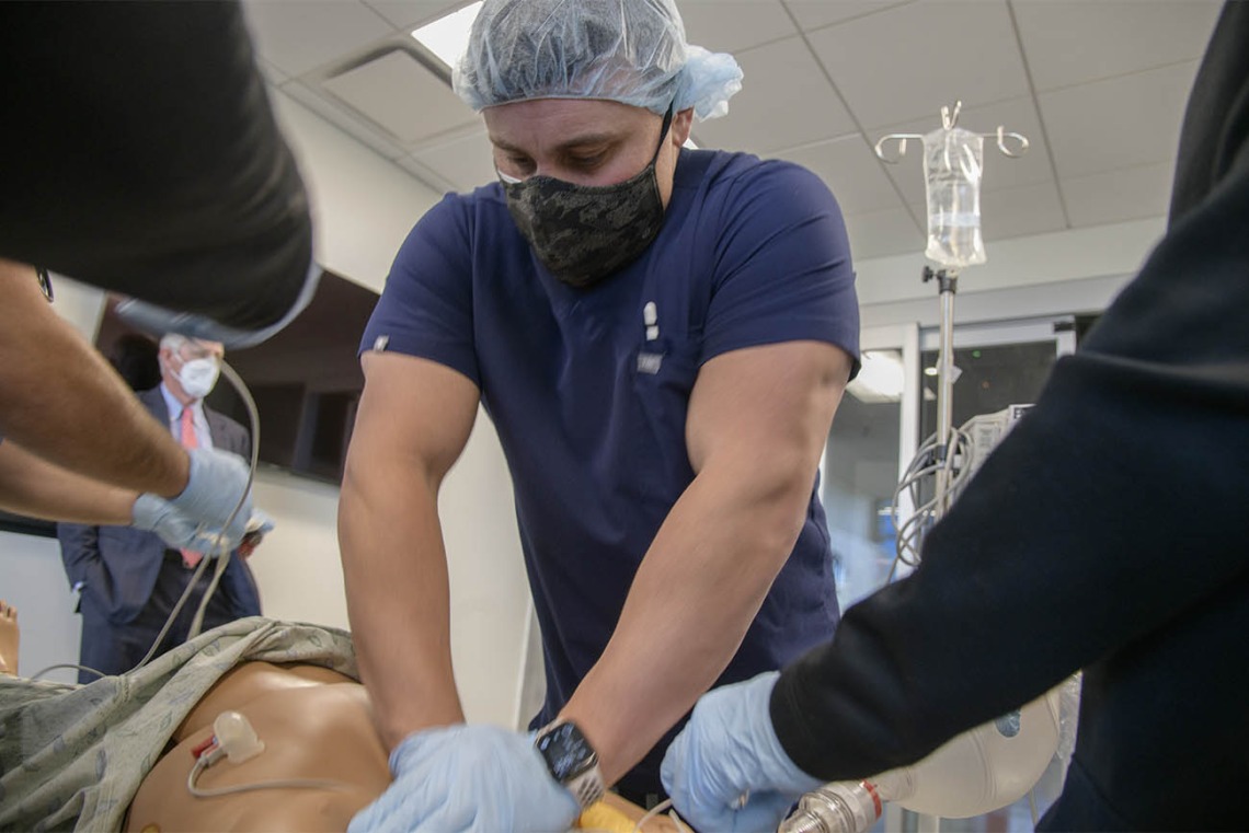 John Mougin, RN, performs chest compressions on a manikin during a CRNA critical skills intensive simulation in the Arizona Simulation Technology and Education Center, while University of Arizona President Robert C. Robbins, MD, observes in the background. 