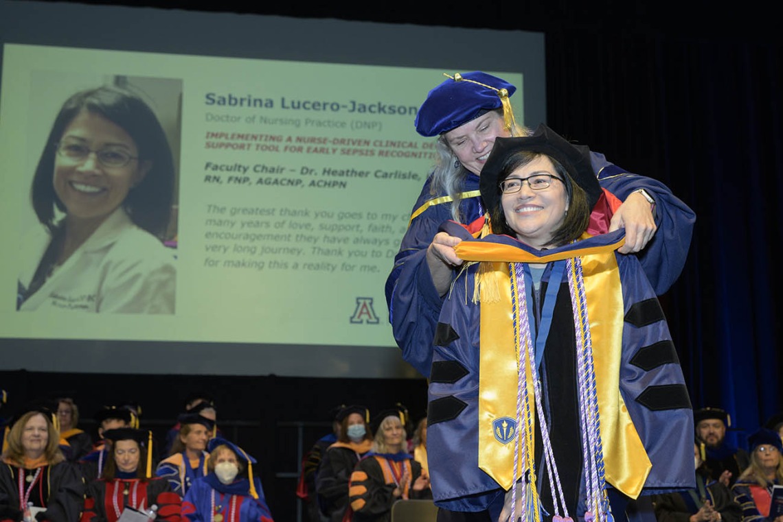 Sabrina Lucero-Jackson is hooded by associate professor Heather L. Carlisle, PhD, DNP, RN, FNP, AGACNP, CHPN, during the UArizona College of Nursing fall convocation for earning a Doctor of Nursing Practice degree.