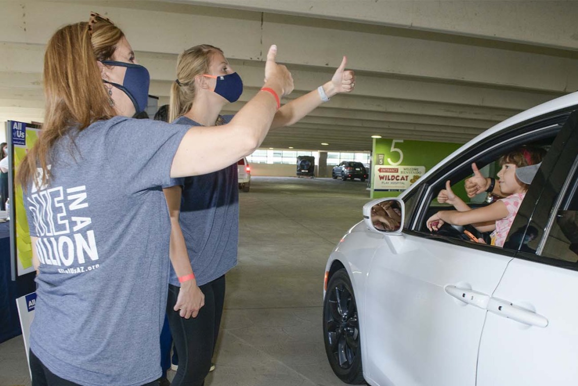Staff from the All of Us Research Program give a thumbs up to a carload of visitors to demonstrate how “hitchhiker’s thumb” is an example of an inherited genetic trait.