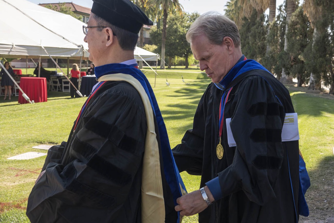R. Ken Coit College of Pharmacy director of graduate studies, Georg Wondrak, PhD, (right) helps adjust the hood on Xinxin Ding, PhD, department head, Pharmacology and Toxicology, before the start of the 2022 spring convocation at Centennial Hall.