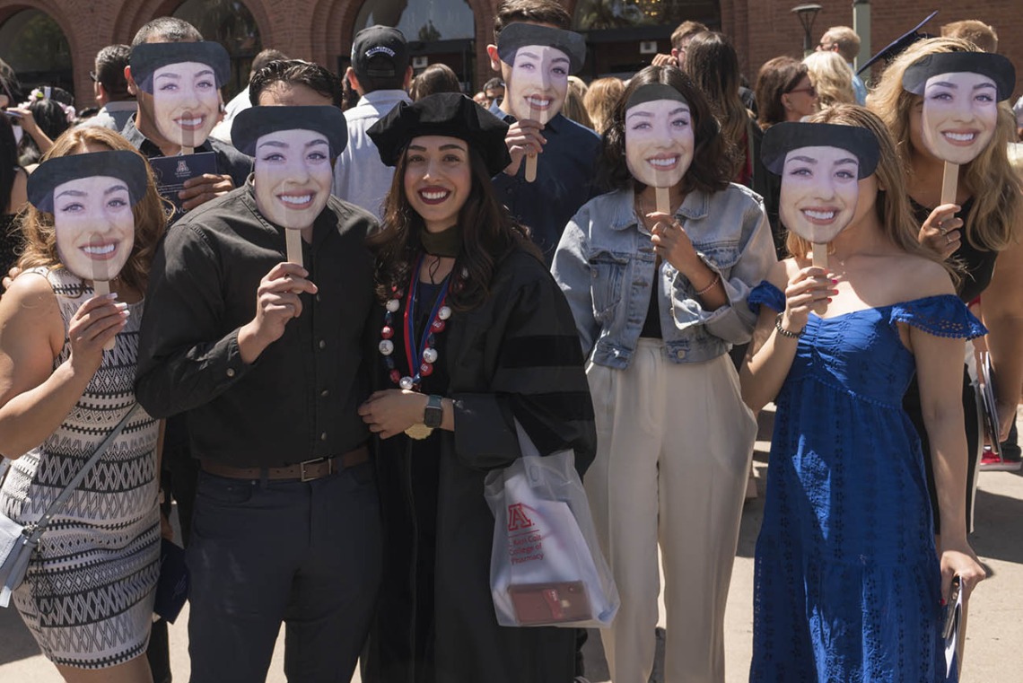 Daisy Arellano, PharmD, poses for a photo with her family – who all hold up photos of her face – after the R. Ken Coit College of Pharmacy 2022 spring convocation at Centennial Hall.  