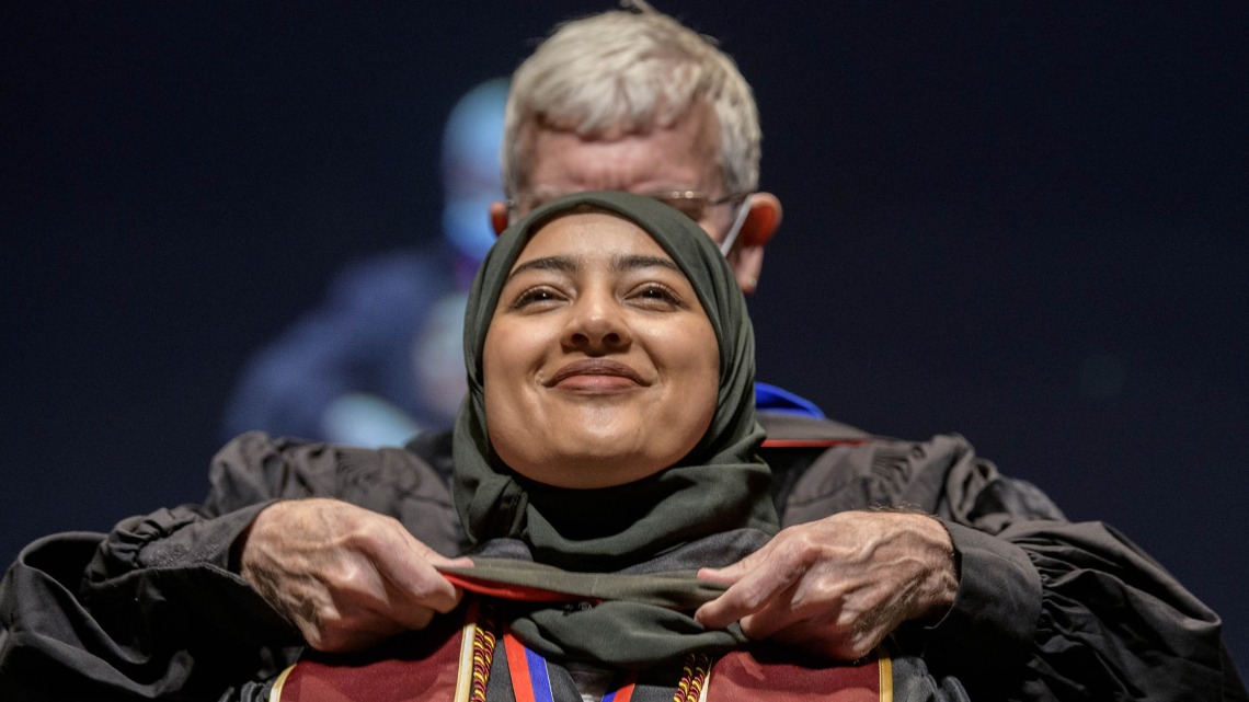 Ahlam Althobaiti, PharmD, is hooded by John Regan, PhD, for earning her Doctor of Pharmacy degree during the R. Ken Coit College of Pharmacy 2022 spring convocation at Centennial Hall.