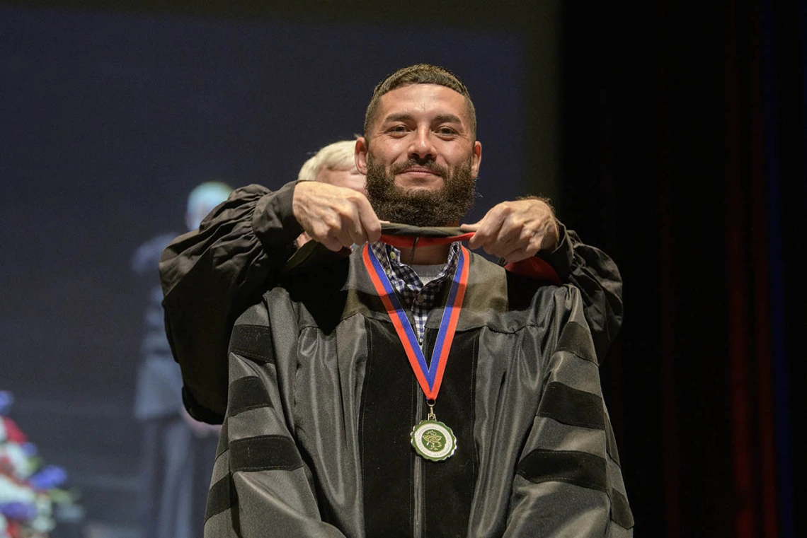 Andy Valencia, PharmD, is hooded by John Regan, PhD, during convocation for earning his Doctor of Pharmacy during the R. Ken Coit College of Pharmacy 2022 spring convocation at Centennial Hall.