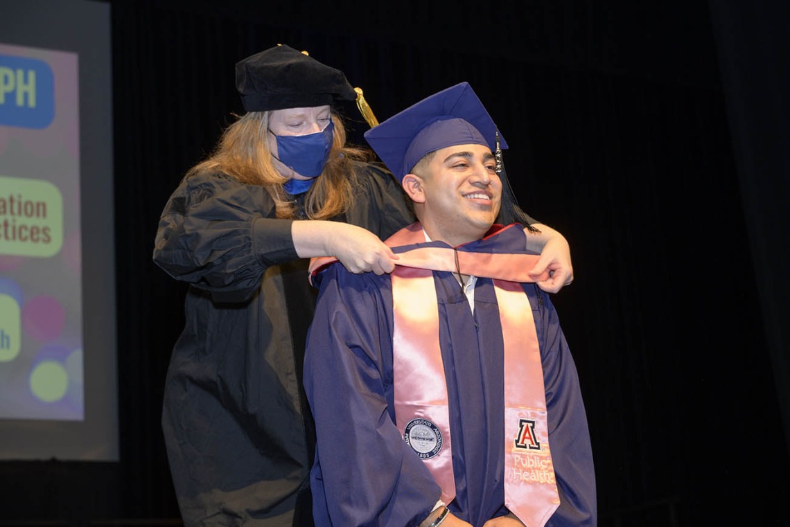 Master of Public Health graduate Martin Caudillo smiles as he is hooded by assistant professor of practice Christina Cutshaw, PhD, during the Mel and Enid Zuckerman College of Public Health fall convocation.