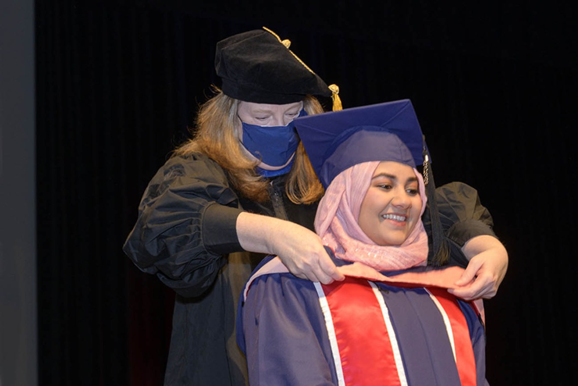 Master of Public Health graduate Javeria Ahmad is hooded by assistant professor of practice Christina Cutshaw, PhD, during the Mel and Enid Zuckerman College of Public Health fall convocation.