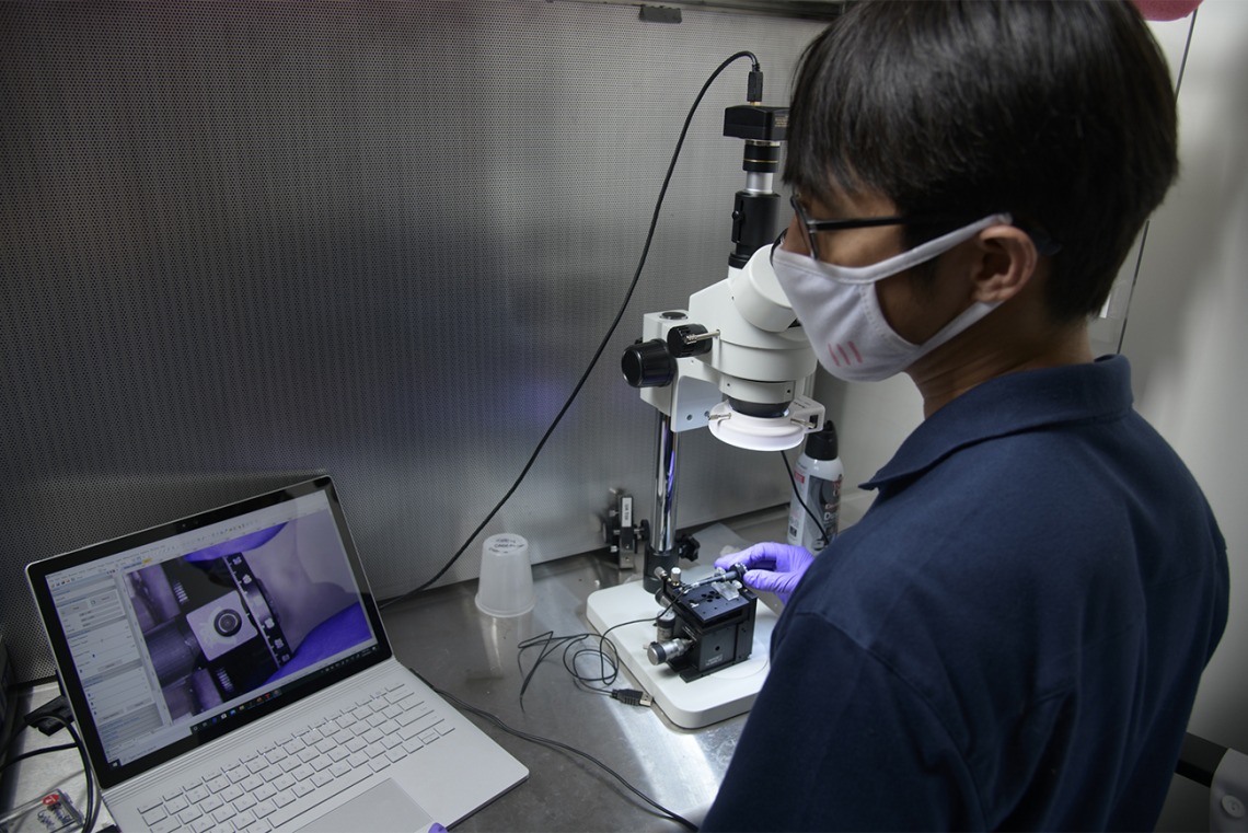 Dongkyun Kang, PhD, uses a microscope and laptop to assist his work on debugging the assembly of a new, handheld microscope to help diagnose skin cancer.