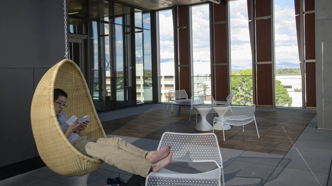 The Health Sciences Innovation Building is filled with cool and creative spaces to study, or just hang around – like this student on the sixth-floor open-air balcony where there are two hanging wicker chairs.