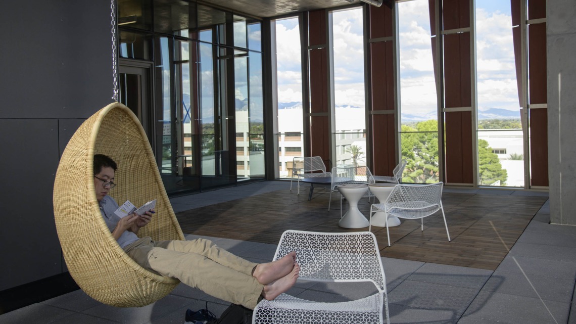 The Health Sciences Innovation Building is filled with cool and creative spaces to study, or just hang around – like this student on the sixth-floor open-air balcony where there are two hanging wicker chairs. 