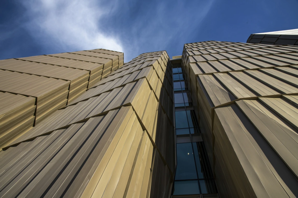 The west side of the Health Sciences Innovation Building features twisting lines of concrete and mesh, which enable light to enter the building, while enclosing elevators and staircases. The angle of the sun shifts the shadows created by the twisting shapes throughout the day.