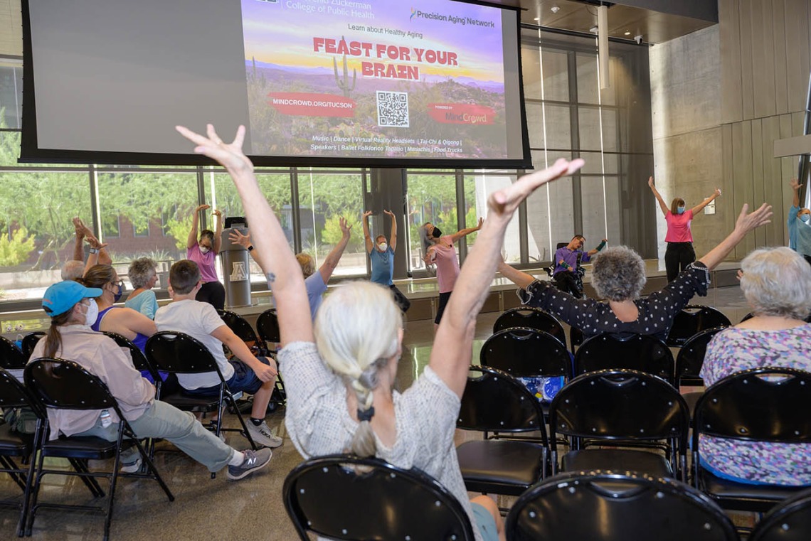 Participants at the inaugural Feast for Your Brain event take part in a group stretch between presentations in the Forum of the Health Sciences Innovation Building.