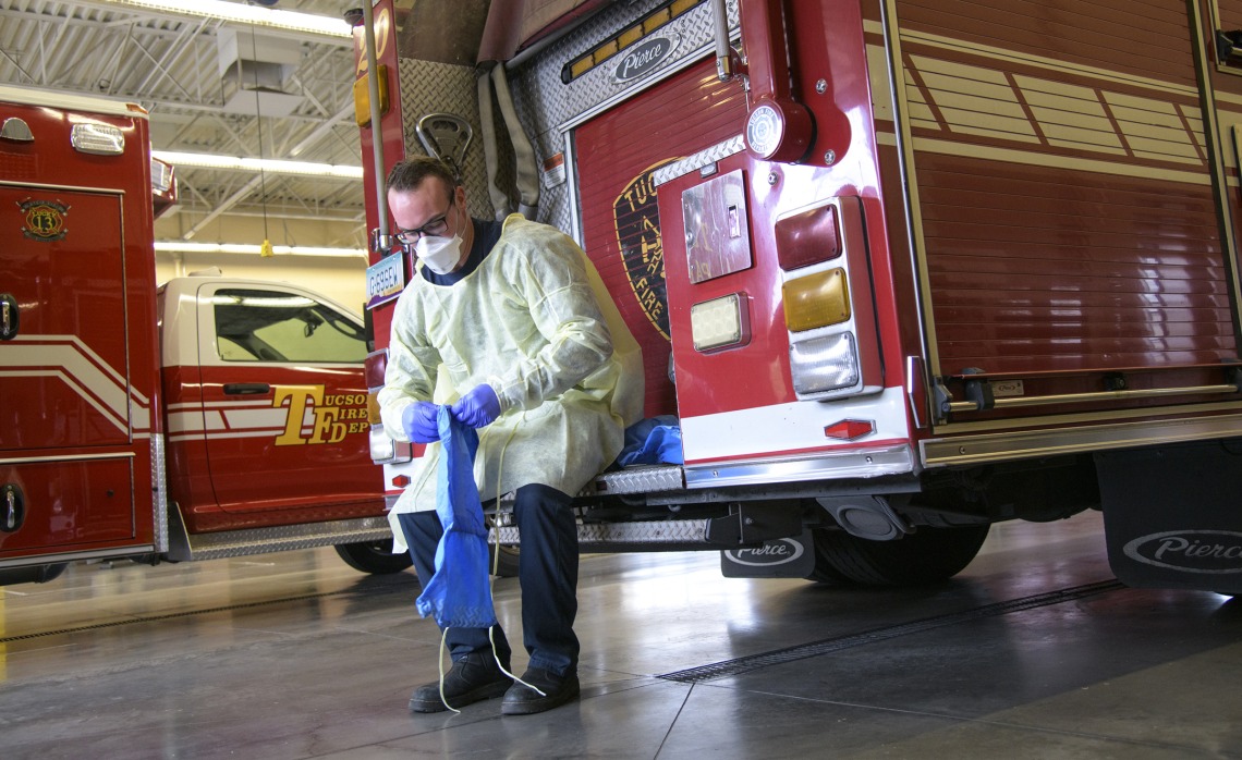 Tucson Fire Department’s Taylor Parrish puts on a protective gown and boot coverings to prevent spread of disease before entering the home a possible COVID-19 patient.