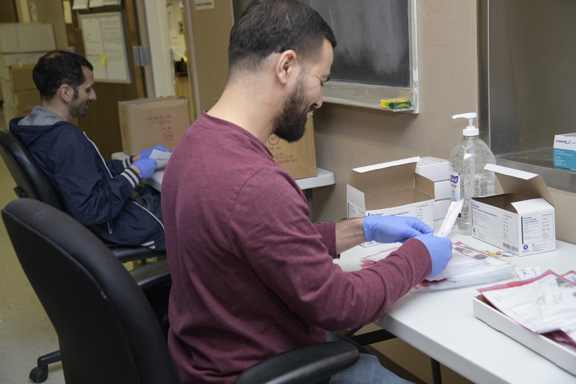 Biorepository laboratory techs Ayman Sam (left) and Brandon Jernigan (right) complete the final step to assemble the COVID-19 sample collection kit.