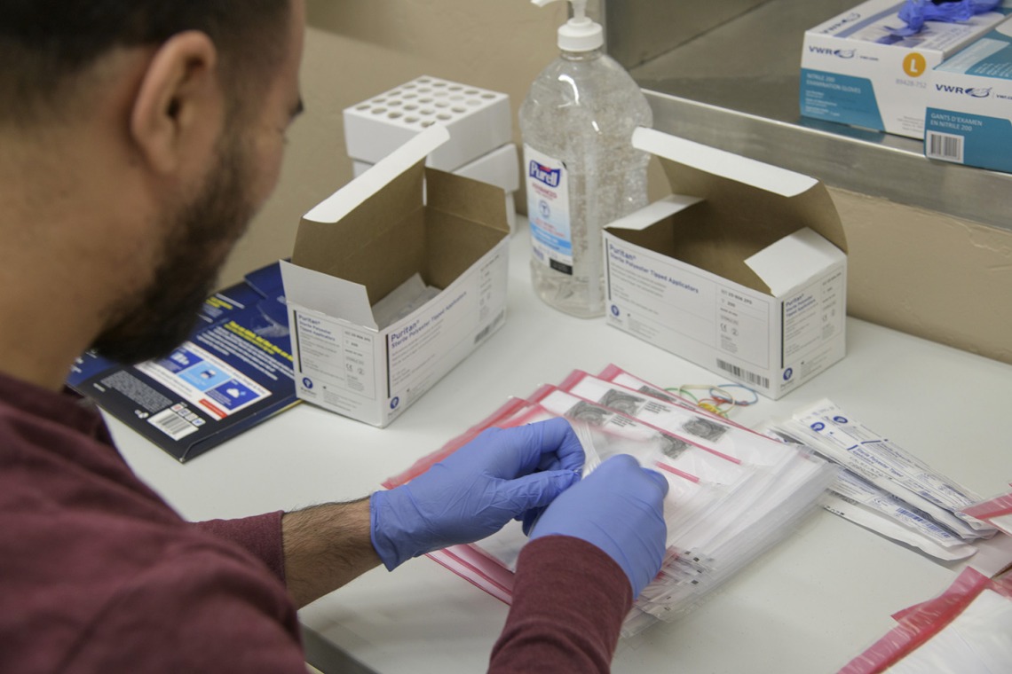 Biorepository laboratory technicians Ayman Sam (left) and Brandon Jernigan (right) complete the final step to assemble a COVID-19 sample collection kit.