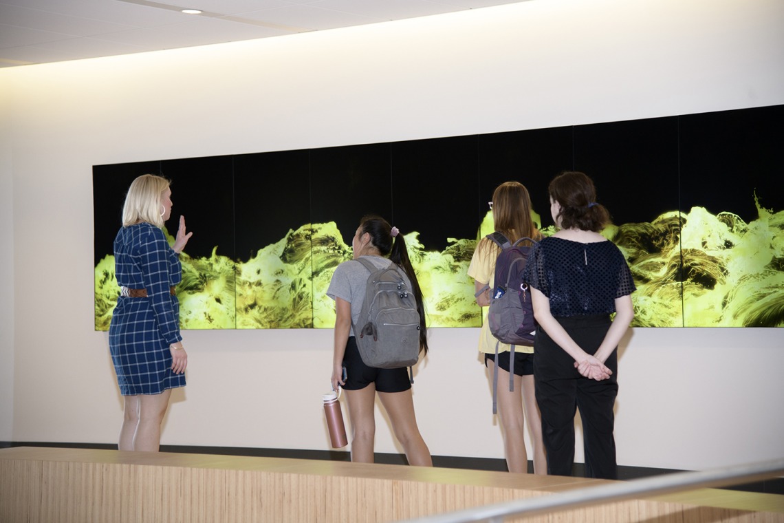Students touring the Health Sciences Innovation Building view “Gold Waves,” a video art installation on the second floor.