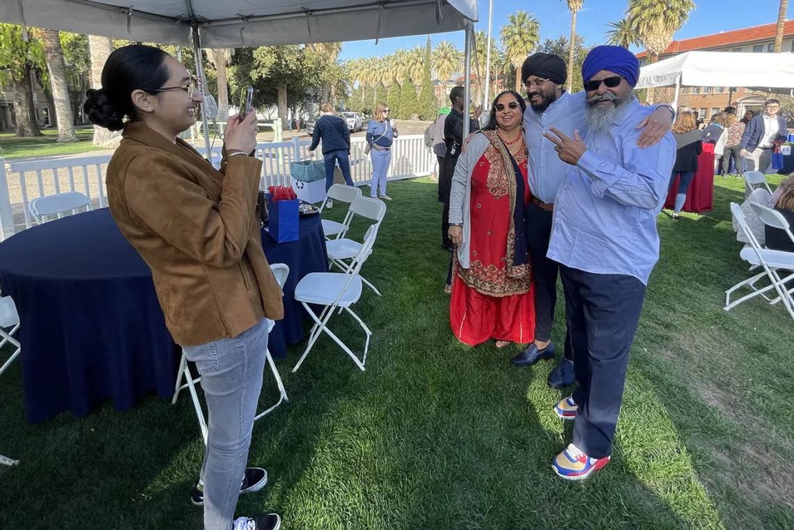 A young man with his parents on either side of him stand for a photo. The two men have headwraps on and beards. 