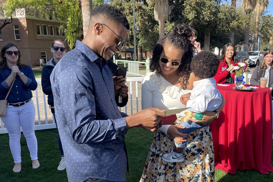 Young dark-skinned doctor shows his match day envelop to his wife and child.