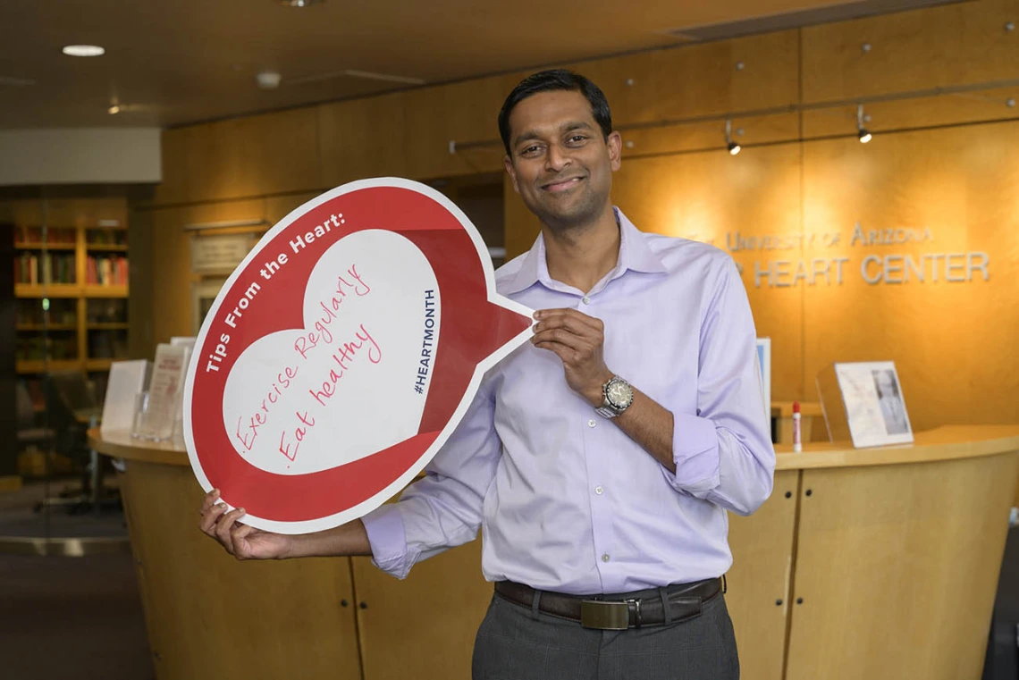 Man with brown skin and short dark hair wearing a button-up shirt holds a heart sign. 